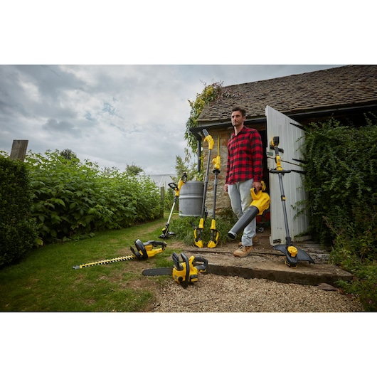 STANLEY SFMCHT855M1 garden tools group shot outdoors, featuring hedge trimmer, chainsaw, blower, and string trimmer.