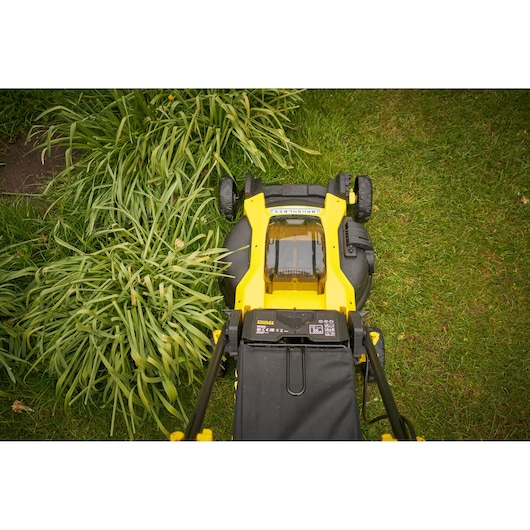 Photo of STANLEY SFMCMW2651M lawn mower on grass, top view showing yellow and black design and battery cover.