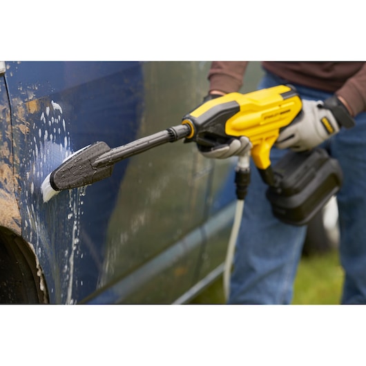 STANLEY SFMCPC93B portable pressure washer cleaning a blue vehicle with soap, close-up angle.