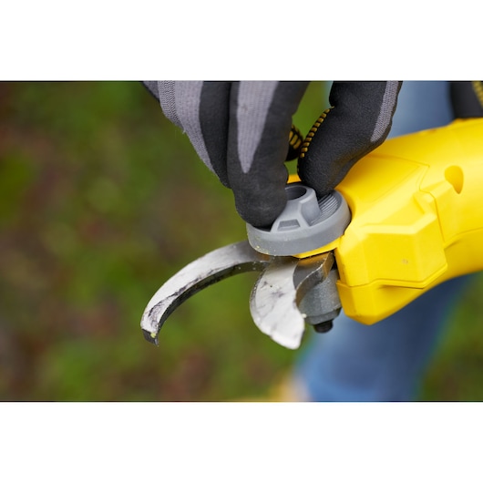 STANLEY SFMCPP32B pruner close-up showing blade maintenance with glove, outdoor setting.