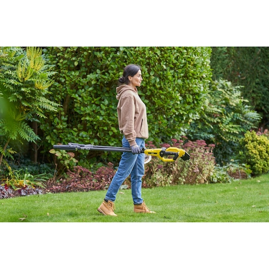 Person carrying STANLEY SFMCPP632D1 pole pruner in a garden, side view, with greenery in the background.