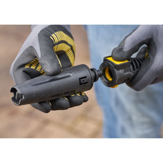 STANLEY SFMCPW1500B hose connector attachment held by gloved hands, close-up outdoor view.