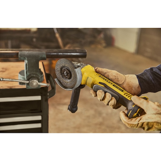 Photo of STANLEY SFMCS310B angle grinder in use, yellow and black body, grinding metal pipe in workshop.