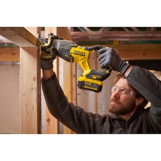 Photo of STANLEY SFMCS311B-XJ cordless reciprocating saw cutting wood, held by person wearing gloves.