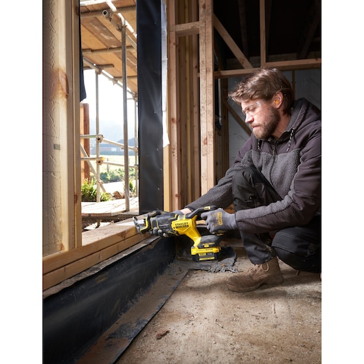 Photo of STANLEY SFMCS311B-XJ cordless reciprocating saw in use at a construction site, cutting wood near a window frame.