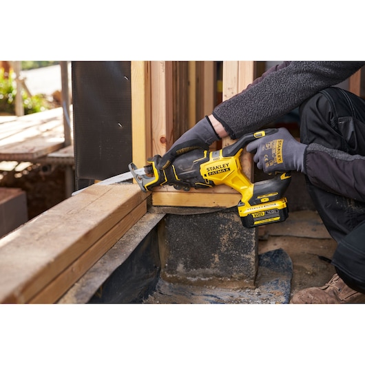 Stanley SFMCS311B-XJ cordless reciprocating saw cutting wood in construction setting, side angle.