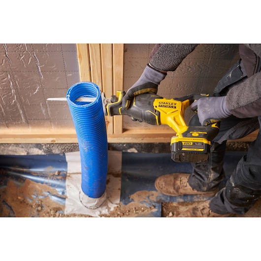 STANLEY SFMCS311B-XJ reciprocating saw cutting blue corrugated pipe, construction setting, side angle.