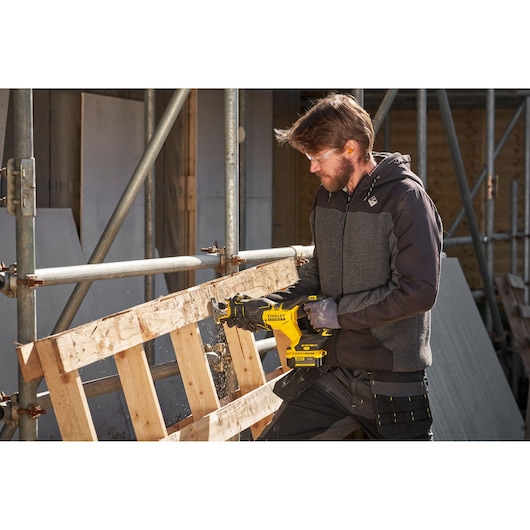 STANLEY SFMCS311B-XJ cordless reciprocating saw cutting wooden pallet outdoors, construction site setting.