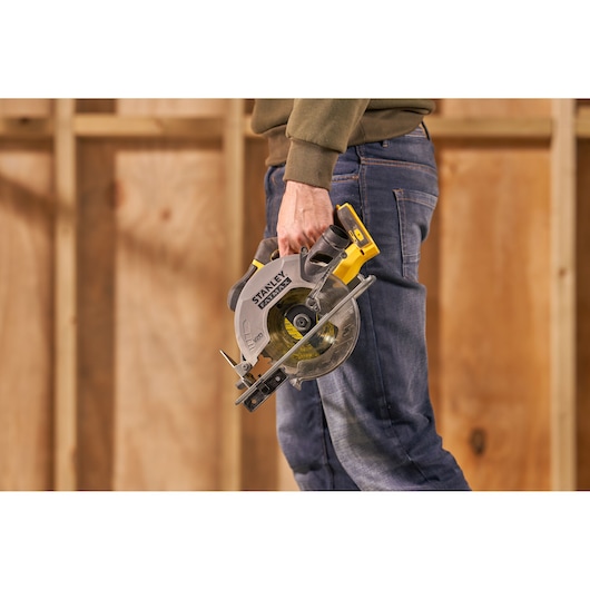 Photo of a person holding a STANLEY SFMCS500M1S circular saw, yellow and black, used for woodworking.