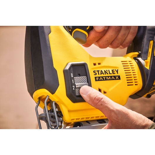 STANLEY SFMCS600B jigsaw close-up, showing hand adjusting speed control switch on yellow and black body.