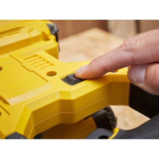 Stanley SFMCS701B yellow power tool close-up showing a finger pressing the black button.