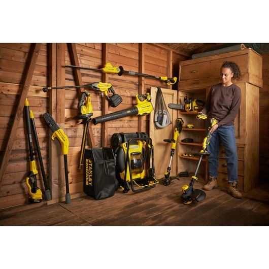 STANLEY SFMCST933B garden tools displayed in wooden shed, one person holding a string trimmer.