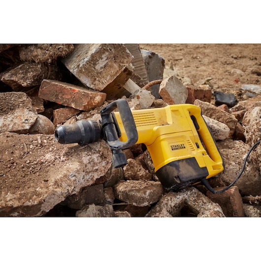 STANLEY SFMEH230K-QS demolition hammer resting on rubble, yellow body with black handle, side view.