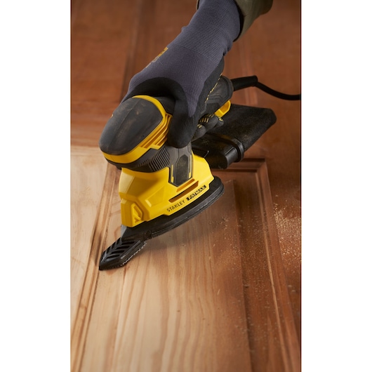 Stanley SFMEW210S sander, yellow and black, in use on wood, close-up at an angle.