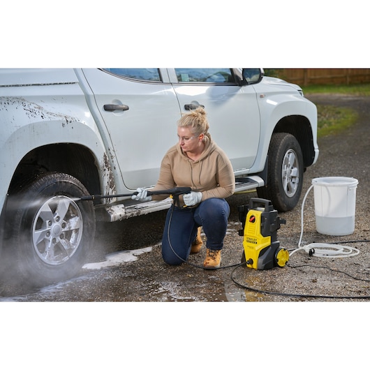 STANLEY SFMPW1740 pressure washer in use cleaning a muddy white pickup truck wheel outdoors.