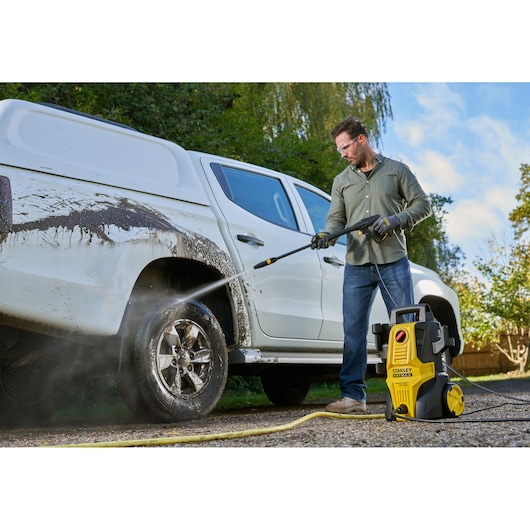 STANLEY SFMPW1740 pressure washer cleaning muddy white pickup truck outdoors.