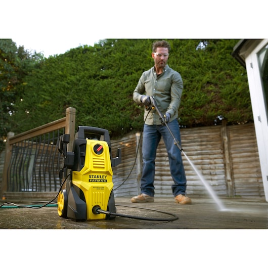 Stanley SFMPW1740 pressure washer in use outdoors, yellow and black, photographed from a front angle.