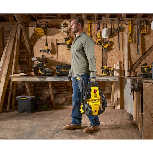 Stanley SFMPW1740 pressure washer held by person in workshop with woodworking tools.