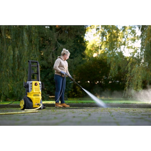 STANLEY SFMPW2000 pressure washer in use outdoors cleaning patio, yellow and black design visible in foreground.