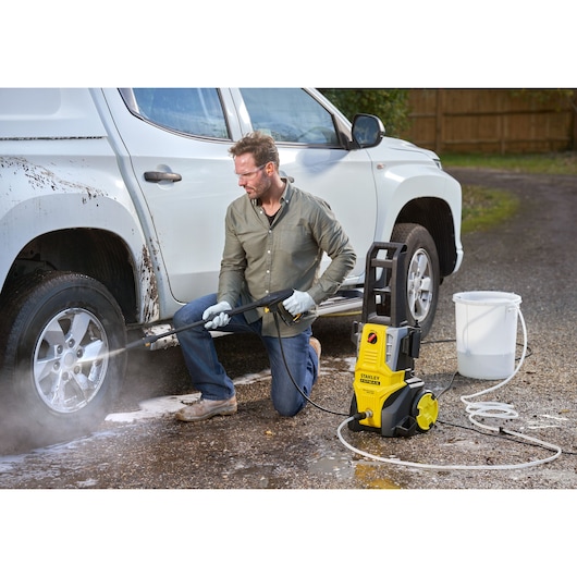 STANLEY SFMPW2000 pressure washer cleaning a white car wheel outdoors, yellow and black unit on ground.