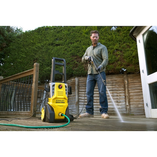 STANLEY SFMPW2000 pressure washer on deck with hose attached, person cleaning wooden surface outdoors.