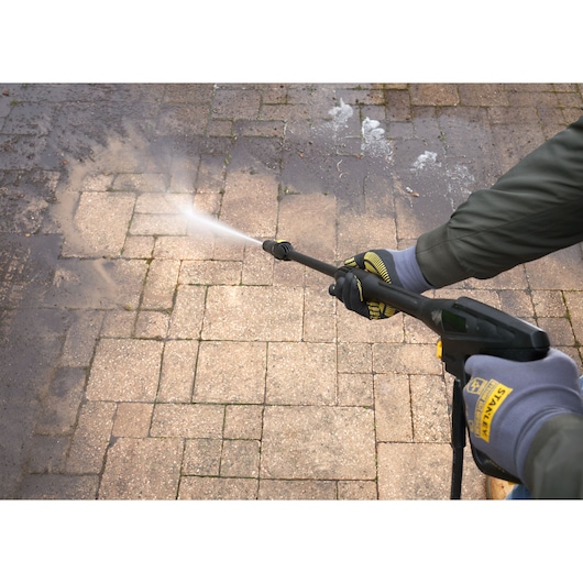 Photo of STANLEY SFMPW2000 pressure washer cleaning dirty outdoor pavement, person wearing STANLEY gloves.