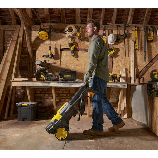 STANLEY SFMPW2000 pressure washer with yellow accents, side view, being wheeled by a person in a workshop.