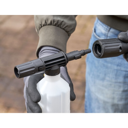 Photo of STANLEY SFMPW2000 pressure washer accessory bottle held in gloved hands, close-up view.