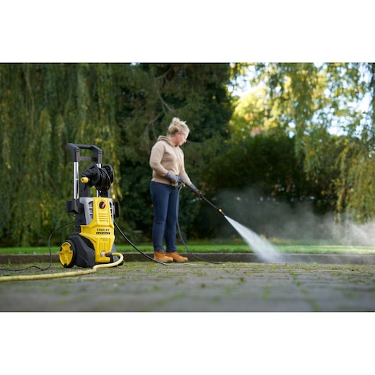 STANLEY SFMPW2400 pressure washer in use cleaning outdoor pavement, yellow and black unit in foreground.