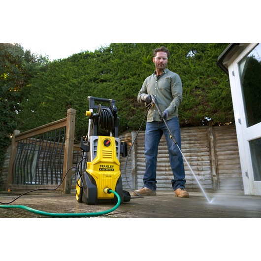 STANLEY SFMPW2400 pressure washer in use outdoors by a person cleaning a wooden deck.