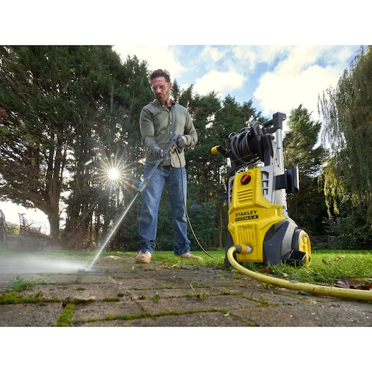 Stanley SFMPW2400 pressure washer in use outdoors, cleaning patio with yellow hose and spray wand.