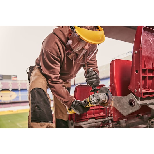 STANLEY STA32637 angle grinder in use cutting metal stadium seat armrest, close-up action shot.