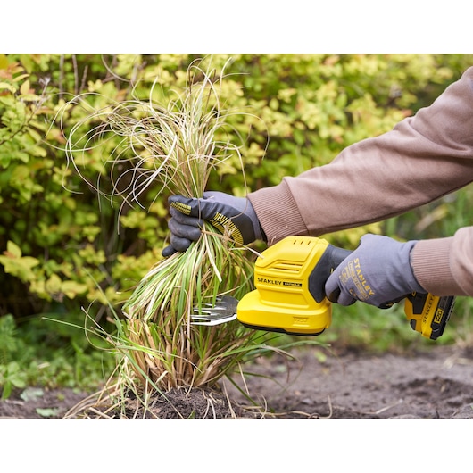 Photo of STANLEY STCSS20B grass shear in use, yellow tool held by gloved hands trimming garden grass.