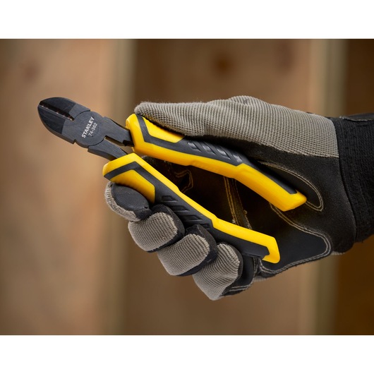 STANLEY STHT0-74362 diagonal cutting pliers with yellow handles held in gloved hand, close-up.