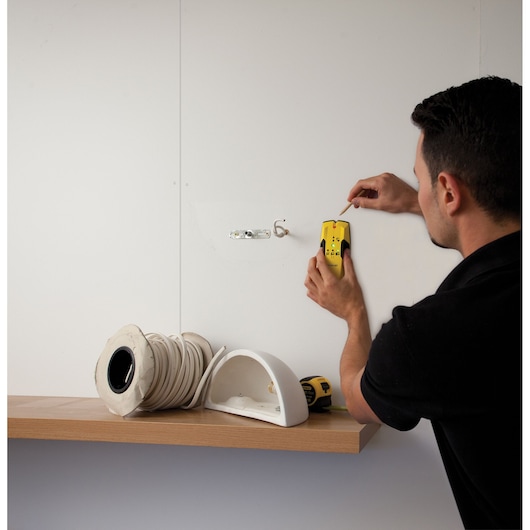 STANLEY STHT0-77404 wall scanner held by person on white wall above shelf with cable and drill, front angle.
