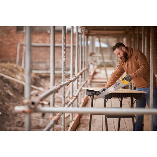 STANLEY STHT1-20352 hand saw in use on a construction site, cutting wood on a sawhorse table.