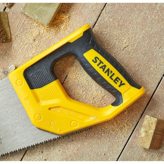 STANLEY STHT1-20352 hand saw with yellow and black handle on wooden surface with sawdust.