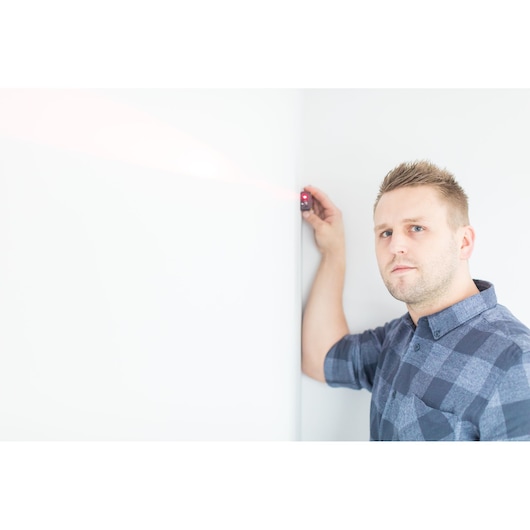 Stanley STHT1-77032 laser distance measurer in use against a white wall, photography product category.