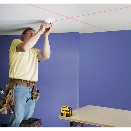 STANLEY STHT1-77341 photography of yellow laser level casting red lines for ceiling installation.