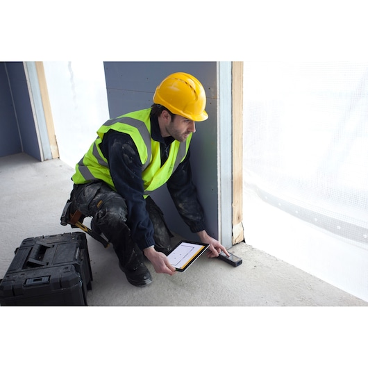 STANLEY STHT1-77347 laser distance measurer in use at construction site, worker wearing yellow vest and helmet.