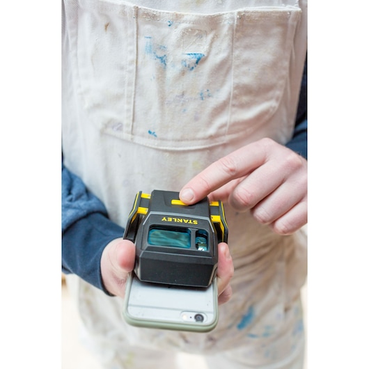 Photo of STANLEY STHT1-77366 laser level on a smartphone, held by a person in paint-stained overalls.