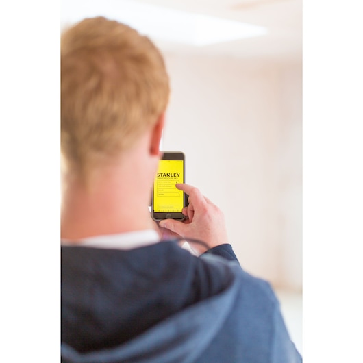Photo of a person using a mobile phone to operate the STANLEY STHT1-77366 laser distance measurer app.