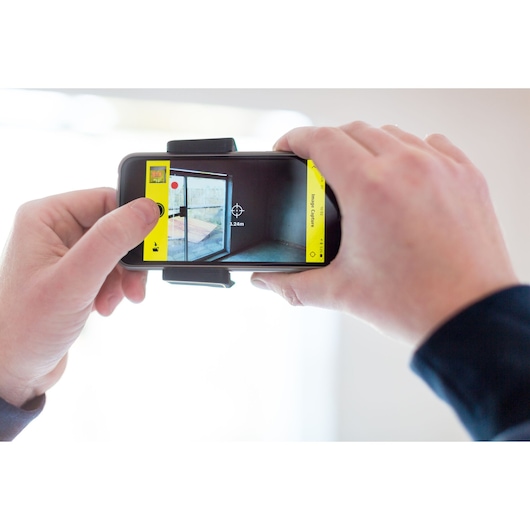 STANLEY STHT1-77366 photography device showing smartphone measuring room distance on screen.