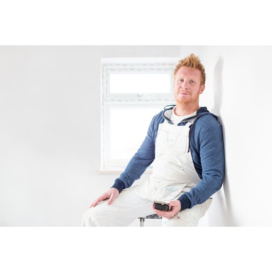 Photo of a person in painter’s overalls holding STANLEY STHT1-77366 photography tool, sitting near a white wall.