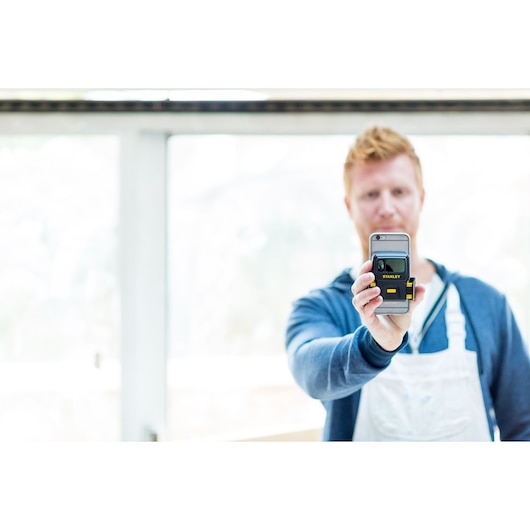 Photo of STANLEY STHT1-77366 electronic laser level held by person in workshop setting.