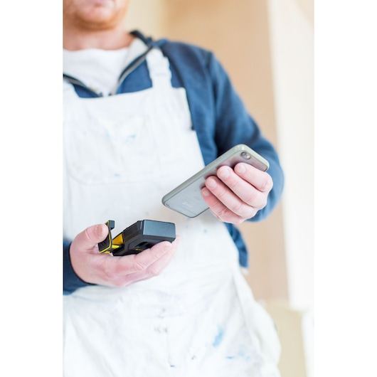 STANLEY STHT1-77366 photography, person in white coveralls holding laser distance measurer and smartphone.