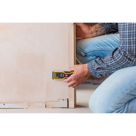 STANLEY STHT1-77409 laser distance measurer in use against a wall during measurement, user in casual workwear.