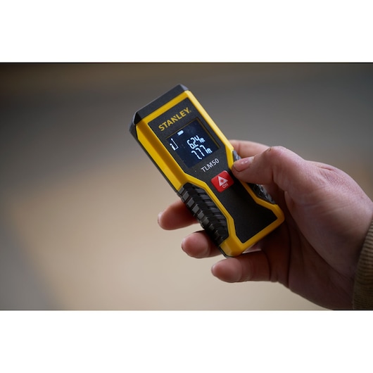 Photo of STANLEY STHT1-77409 laser distance measurer held in hand, yellow and black with digital display.