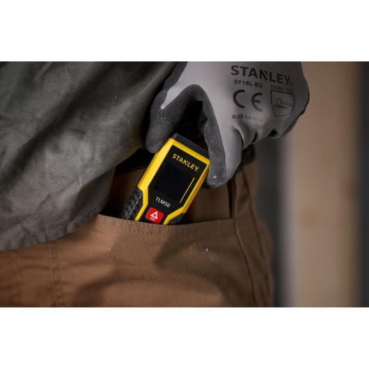 STANLEY STHT1-77409 laser distance measurer TLM50 being placed in a pants pocket by a gloved hand.