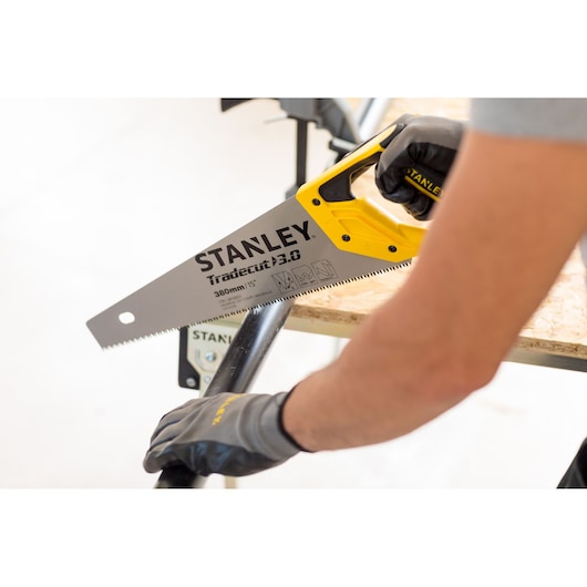 STANLEY STHT20348-0 hand saw with yellow handle cutting black pipe, gloved hand holding saw.